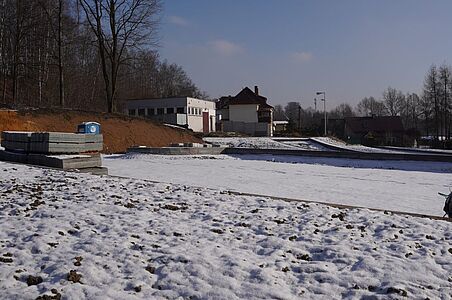Płaski teren pod budowę ze stosami płyt betonowych na tle skarp i budynków