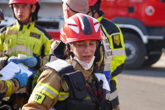 Kobieta ze straży PSP patrzy w dół. Za nią inni rozmawiają ze sędzią