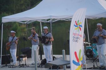 Na pierwszym planie po prawej stronie widoczna flaga Festiwalu Górnej Odry. W tle, na pomoście pod namiotem, gra sześcioosobowy zespół muzyczny w marynarskich koszulkach