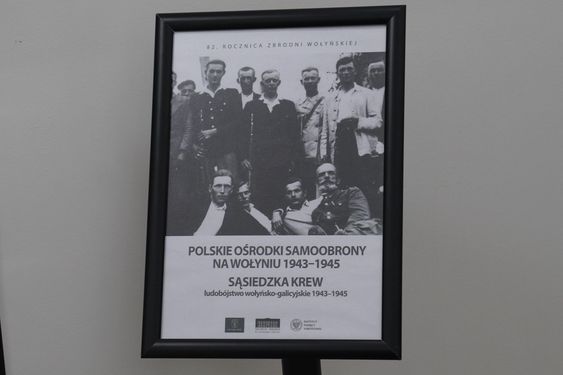 Plakat w czarnej ramie z archiwalnym zdjęciem, zatytułowany „Polskie ośrodki samoobrony na Wołyniu 1943–1945. Sąsiedzka krew”