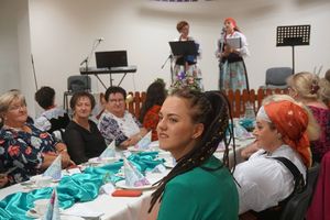 Kobiety zgromadzone w salce, 2 panie w strojach ludowych na scenie