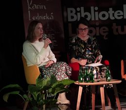 link zewnętrzny, otwarcie w nowej karcie Karin Lednická móiąca do mikrofonu, obok tłumaczka, przed nimi stolik z napojami.