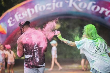 Dziewczyna o zielonych włosach rzuca różowym proszkiem holi w plecy mężczyzny podczas imprezy pod szyldem „Eksplozja Kolorów”