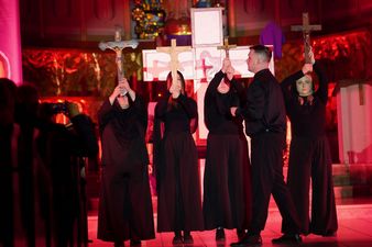 Osoby ubrane na czarne trzymają krzyże wysoko nad głowami, w tle wizerunek krzyża