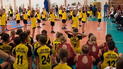 Młodzi uczniowie w strojach sportowych stoją na środku hali podczas występu, przed nimi siedzą pozostali uczestnicy akademii