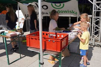 Stoisko Eko Jakość dla środowiska, na pierwszym planie pomarańczowy pojemnik, w dali dzieci stojące wokół stoiska