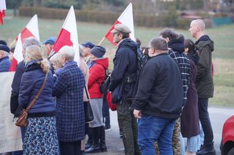 Kobiety i mężczyźni trzymający polskie flagi wokół pomnika upamiętniającego żołnierzy wyklętych