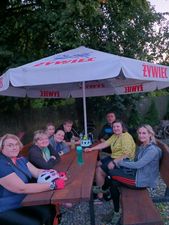 Grupa ludzi siedzi przy ławie pod parasolką