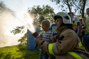 Strażak i dziecko wspólnie używają węża strażackiego.
