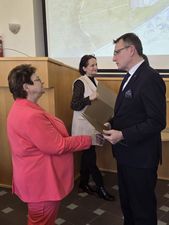 kobieta w koralowym garniturze otrzymuje gratulacje od Prezydenta Michała Urgoła