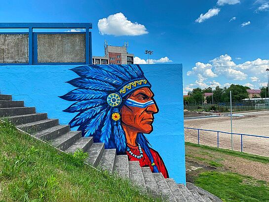 Mural na niebieskiej ścianie obok betonowych schodów przedstawia profil głowy Indianina w imponującym pióropuszu