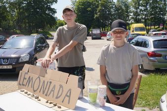 Dwoje nastolatków sprzedających napoje przy stoisku z kartonowym, odręcznym napisem „LEMONIADA”
