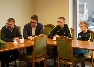 Trenerzy i zawodnicy siedzacy przy stole, słuchaja w skupieniu