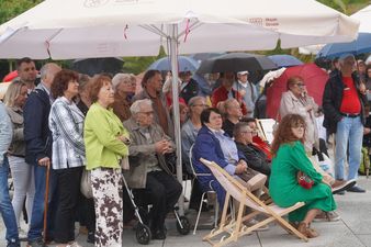 Widzowie stojący i siedzący w dużej grupie pod parasolami