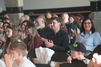 zaproszeni na wernisaz goście siedzą na krzesłach 