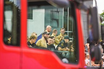 Widzowie obserwowani z wnętrza lub przez szybę czerwonego wozu strażackiego, opierający się o barierki widowni