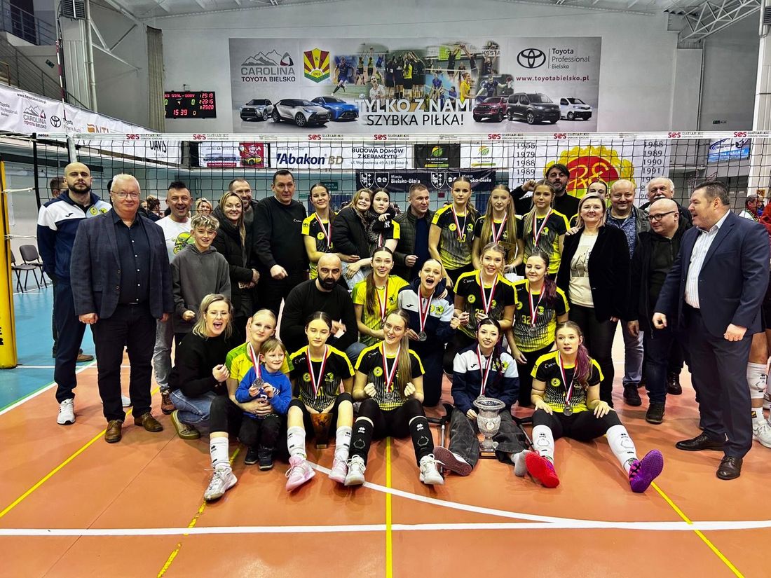 Drużyna srebrnych medalistek pozująca do zdjęcia z medalami i pucharami, obok trenerzy i działacze