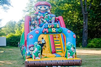 Duży, kolorowy dmuchany zamek z motywem „Super Mario”, po którym wspinają się dzieci