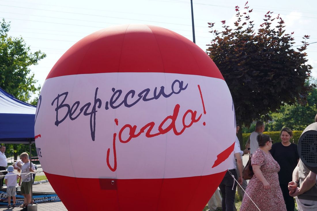 Duża, czerwono-biała dmuchana kula z napisem „Bezpieczna jazda!”. W tle widać przechodniów i fragmenty stoisk profilaktycznych