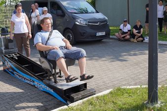 Mężczyzna w letnim stroju siedzi w fotelu przypięty pasami na pochylni symulatora zderzeń, przygotowując się do testu w kontrolowanych warunkach