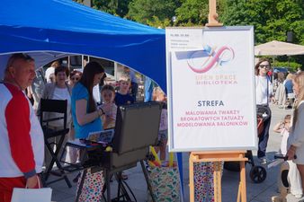 Plansza z napisem kulturalny open space strefa malowania twarzy w tle ludzie