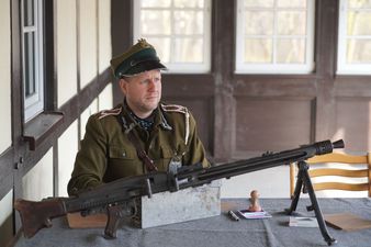 Mężczyzna w stroju wojskowym, na stole przed nim prezentowany jest zabytkowy karabin