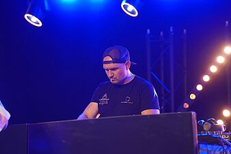 DJ w czapce z daszkiem grający na konsoli w niebieskim oświetleniu scenicznym