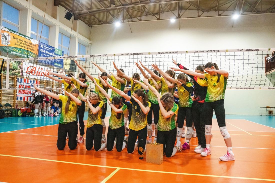Drużyna JKS-u pozuje na tle siatki w geście wyprostowanych w górę i prawa stronę ramion na znak zdecydowanego zwycięstwa