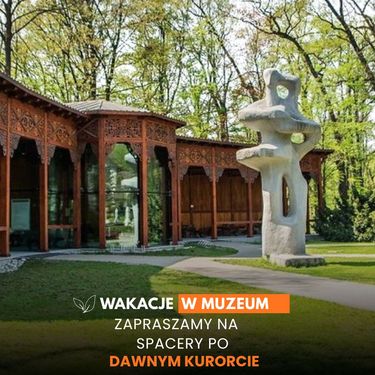 Wakacje w muzeum. Zapraszamy na spacery po dawnym kurorcie. W tle widać zabytkowy, drewniany budynek pijalni wód z rzeźbionymi detalami oraz nowoczesną, jasną rzeźbę o nieregularnym kształcie stojącą w parku