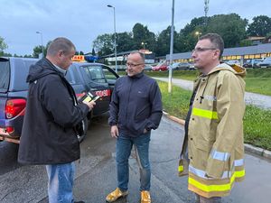 Trzech mężczyzn w tym Prezydent Miasta oraz osoba w umundurowaniu strażackim, rozmawiają na parkingu obok oznakowanego pojazdu straży pożarnej