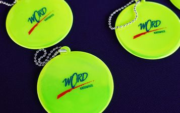 Trzy jaskrawozielone, okrągłe odblaski z niebiesko-czerwonym logo WORD Katowice, leżące na ciemnym tle