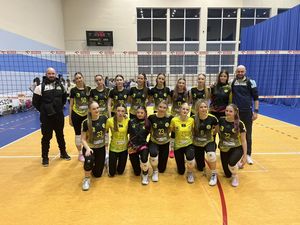 Grupowe zdjecie juniorek JKS-u z trenerami na tle siatki