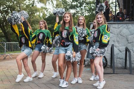 Dziewczęcy zespół cheerleaderek w zielono-czarnych bluzach sportowych pozuje z błyszczącymi, srebrnymi pomponami