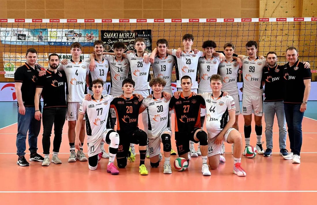 Drużyna juniorów Akademii Talentów pozująca z trenerami przy siatce na parkiecie