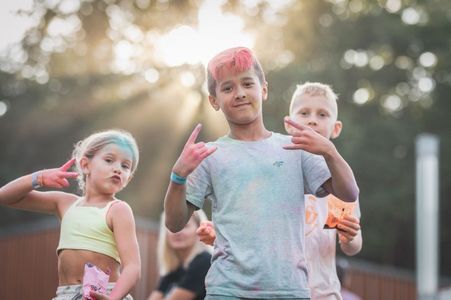 Trójka dzieci umazanych kolorowymi pyłami pozuje do zdjęcia, pokazując rockowe gesty rękami