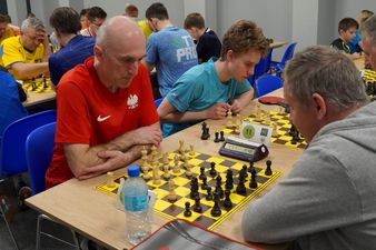 Dwaj dorośli męzczyźni na pierwszym planie, skupieni na grze w szachy