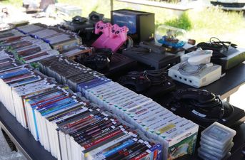 Gry na różne konsole (m.in. PS3, Nintendo DS) oraz retro konsole i różowe pady ułożone w rzędach na stole wystawowym
