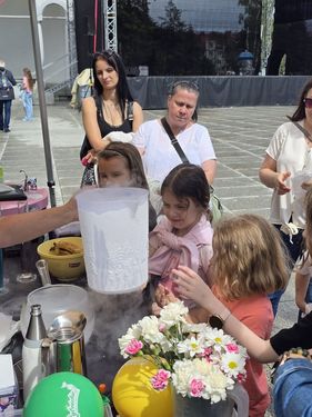 Zaciekawione dzieci i dorośli obserwujący przygotowywanie napoju z użyciem suchego lodu, z którego unosi się gęsty dym