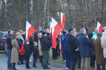 Większa grupa zgromadzona wokół pomnika poświęconego żołnierzom wyklętym, część z nich trzyma polskie flagi