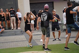 Kobieta w czarnym stroju tańcząca w strefie plenerowej obok innych bawiących się osób