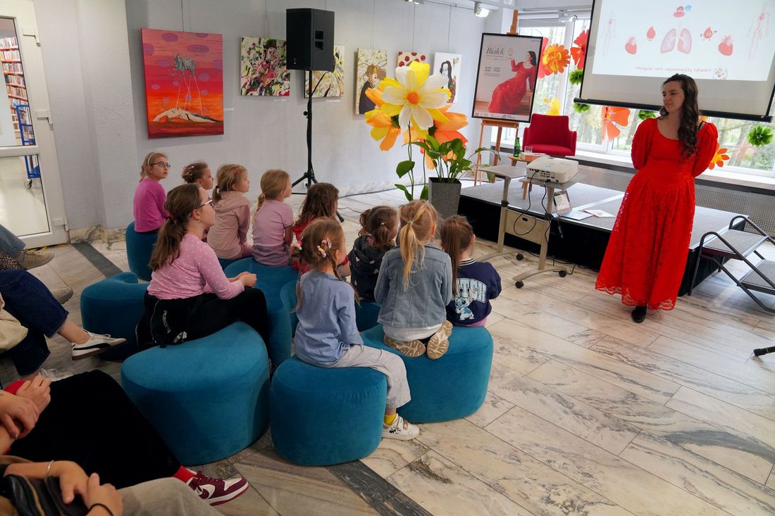 Sonia Białek opowiada o książce przed nią siedzą dzieci w tle ekran i obrazy