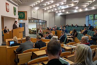 Radni na sali sesyjnej, przemawia przewodniczący rady miasta Piotr Szereda