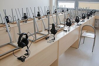 Pracownia językowa ze słuchawkami z mikrofonem umieszczonymi na stanowiskach oraz krzesłami odwróconymi do góry nogami na ławkach