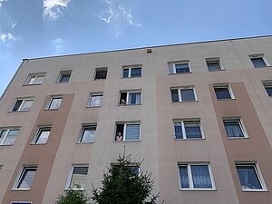 Mieszkańcy bloku wyglądający przez otwarte okna na wyższych piętrach budynku