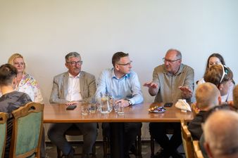 Gestykulujący Marian Janecki podczas rozmowy przy stole, pozostali uczestnicy słuchają go z uwagą