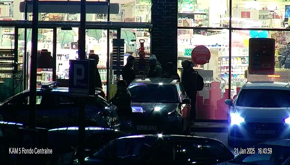 Zdjęcie z kamery 5 Rondo Centralne przedstawia parking, na którym stoją zaparkowane samochody i ludzie.