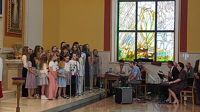 Dziecięcy chór wraz z osobami grającymi na instrumentach.