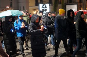 Uczestnicy drogi krzyżowej idą ulicą i trzymają zapalone znicze