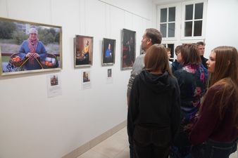 Zwiedzający oglądają serię portretów wystawionych na białej ścianie w galerii sztuki