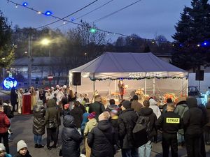 Widok ogólny na wieczorne wydarzenie plenerowe: kobieta przemawia na scenie pod namiotem „Sołectwo Bzie”, a przed nią stoi zgromadzony tłum ludzi